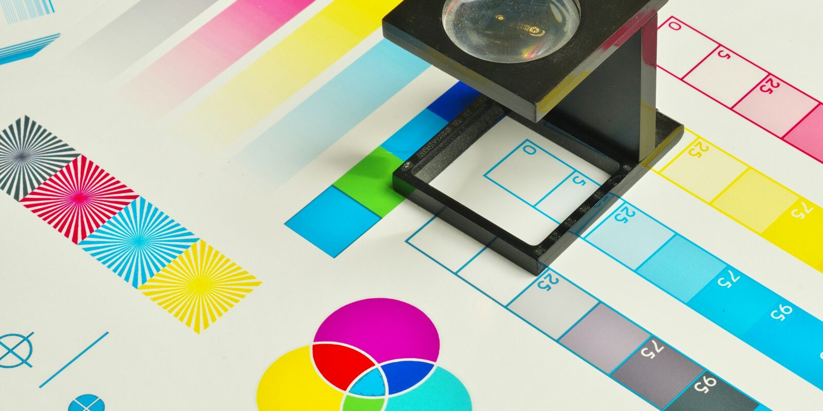 Ein Fadenzähler auf einem Druckkontrollbogen mit CMYK-Farbfeldern und Passkreuzen